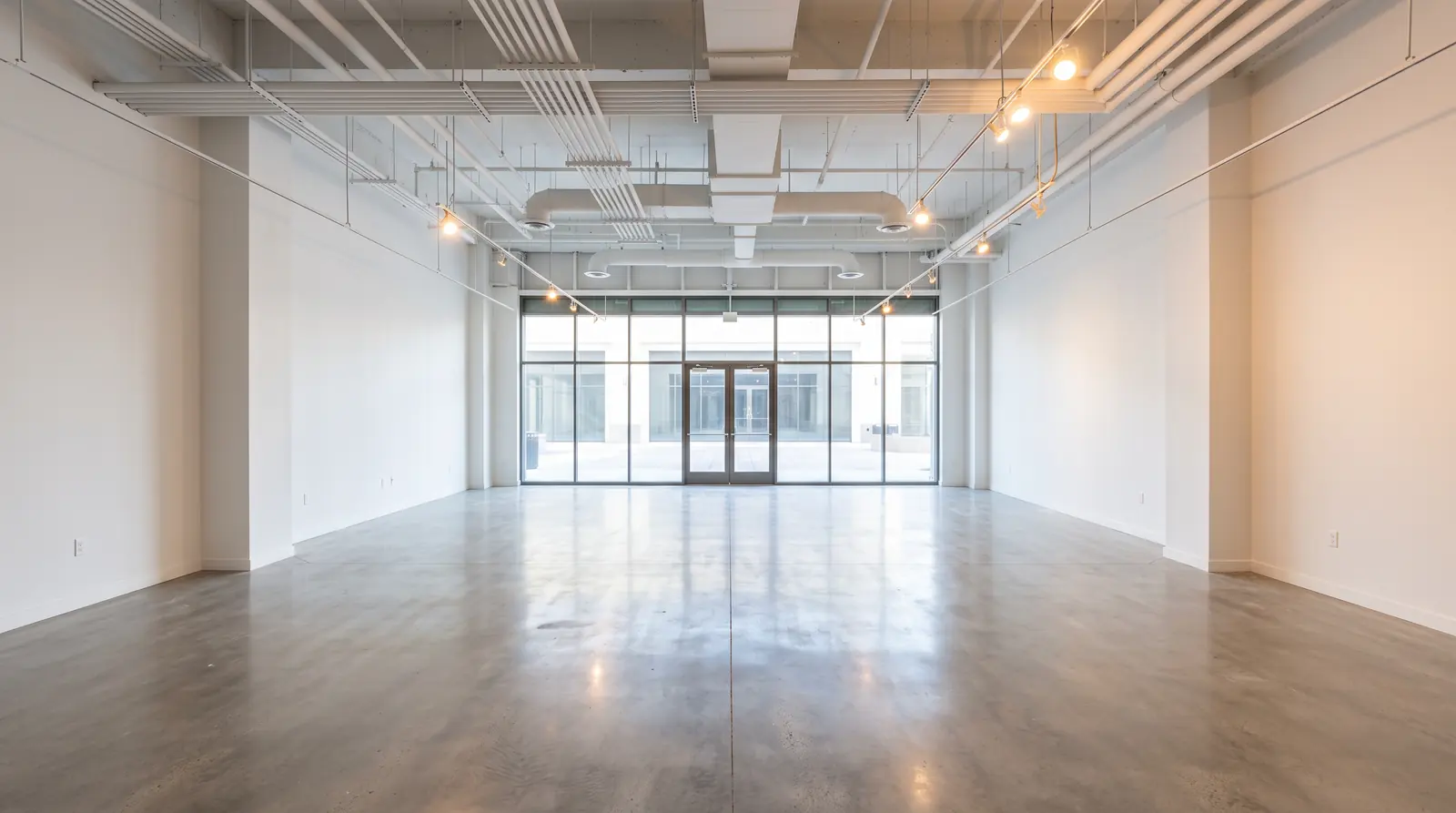 Post-Construction Cleaning | Music City Cleaner A newly built empty retail space cleaned after construction, spotless concrete floor, crystal-clear glass storefront, fresh white walls and warm work lights